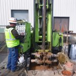 Photo of a mini-sonic drill rig in operation with an upright control panel.